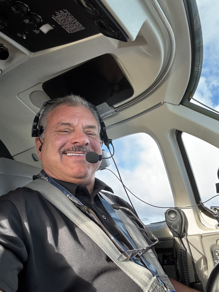 Captain Frank in the cockpit wearing a headset and shoulder harness